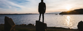 Guy standing on a rock while looking out over water.