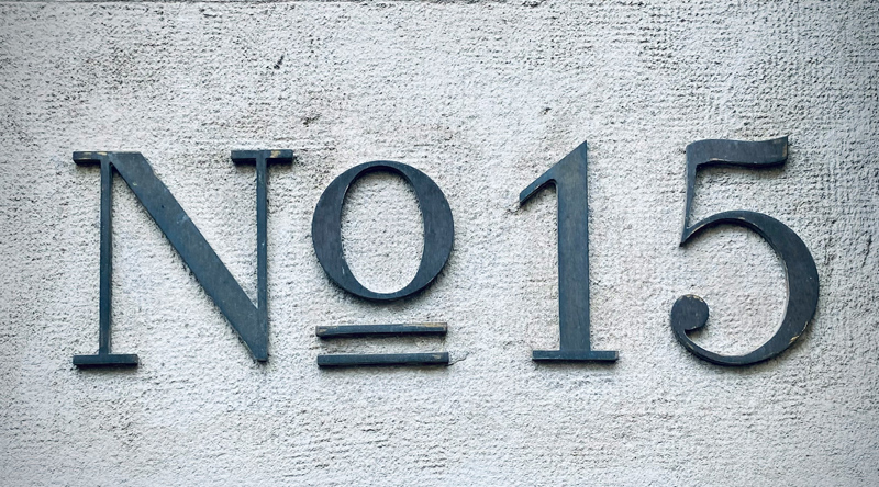 "No. 15" in black wooden text on a stuccoed gray wall.