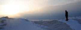 Person standing in the snow and ice as the sun shines on the horizon